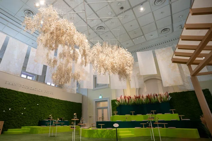 亚洲文明博物馆（Asian Civilisations Museum）举办的《Garden of Senses / 茶苑梦：A Tea Reverie》展览现场，展厅中央设有层层阶梯式绿色装置空间，象征自然与茶园景观，访客可在此驻足体验茶文化的沉静氛围。空间上方悬挂由本地艺术家创作的纸艺装置，层叠的米白色纸叶从天花板垂落，宛如茶叶在空中飘浮，营造宁静而富有诗意的视觉效果。展厅周围摆放传统茶具与艺术展示台，结合现代展览设计与自然元素，呈现融合视觉、触觉与文化体验的沉浸式茶文化空间，让访客重新感受茶作为日常仪式与文化传承的意义。