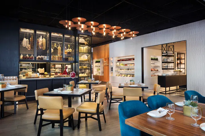 JW Marriott Singapore South Beach 内的 Beach Road Kitchen 餐厅内部环境，灯光温暖、装饰现代，餐桌整齐摆放，氛围舒适宜人。在新加坡去哪里玩？新加坡好玩推荐