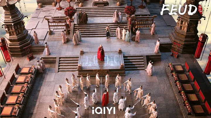 古装剧场景中，身着红衣的人物立于高台中央，周围环绕白衣剑士与群臣，画面展现出《临江仙》中庄严壮阔的古风氛围。临江仙剧照