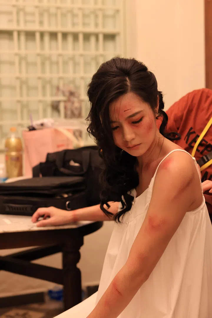 《小娘惹之翡翠山》剧照中，Ferlyn饰演的周红玉身穿白色衣裙坐在室内，手臂与肩膀可见多处伤痕与瘀伤，低头神情落寞。