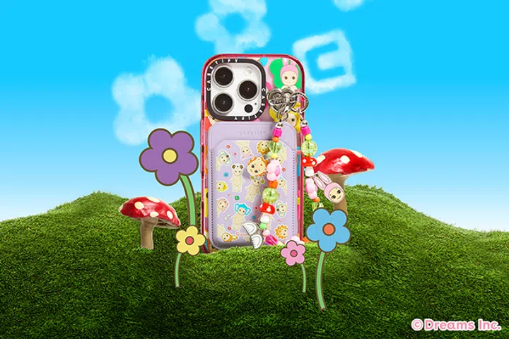 CASETiFY × Sonny Angel联名手机壳与配件展示。图片中是一款印有Sonny Angel小天使图案的iPhone保护壳，搭配紫色卡套、彩色珠串挂链以及Sonny Angel人偶吊饰。背景为绿草地与蓝天，点缀蘑菇和花朵插画，营造童趣梦幻氛围。此系列将Sonny Angel经典可爱造型融入CASETiFY实用配件。