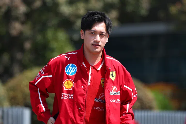 照片中，周冠宇（Zhou Guanyu）身穿红色法拉利车队夹克与队服，上面有Shell、HP、IBM等赞助商标志。他面向镜头，神情专注，在赛场外亮相。作为中国首位F1车手，他是F1亚洲新世代的重要代表。F1赛车手周冠宇，中国第一个F1赛车手。