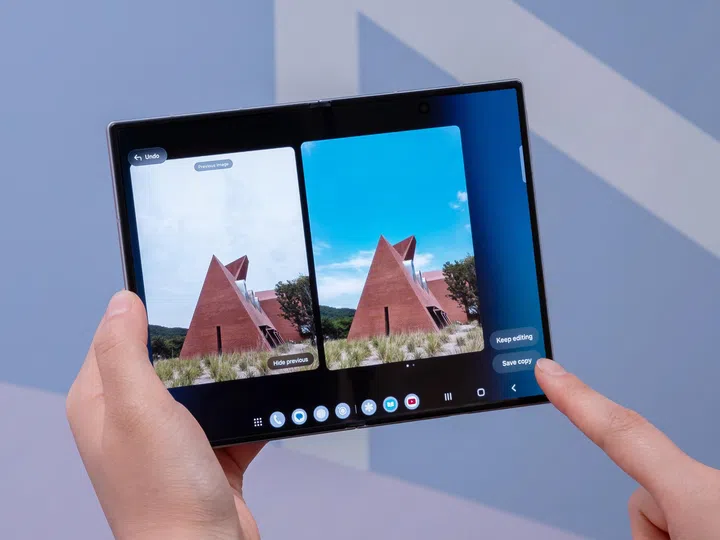 一名用户双手握着展开状态的Samsung Galaxy Z Fold8，正在使用Galaxy AI照片编辑功能。手机屏幕以左右对比方式显示同一张建筑物照片，左侧为原始画面，天空较灰白；右侧则为AI调整后的照片，天空变得更加湛蓝，整体色彩更鲜明，同时保留建筑物与周围景物的细节。屏幕右侧可见“Keep editing（继续编辑）”及“Save copy（储存副本）”按钮，展示Galaxy AI能够直接在手机内进行智能修图、优化色彩及快速编辑照片，无需切换至其他修图应用程序。背景采用蓝紫色渐层灯光，整体画面突显Galaxy Z Fold8的大屏幕编辑体验及AI修图功能。