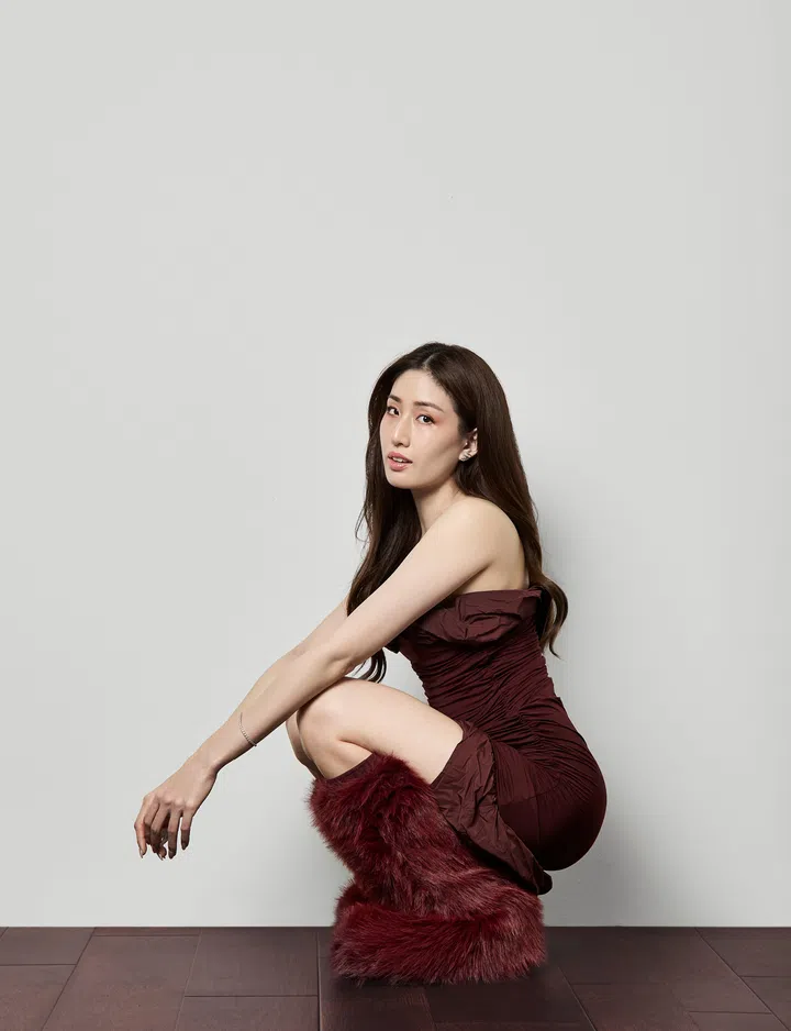 Kimberly Haley Wang 为《The Millennial Talk》专访拍摄的肖像照，她身穿酒红色无肩带贴身洋装，搭配同色系毛绒长靴，侧身蹲坐在深色木质地板上，身体微微前倾，双臂自然垂放，直视镜头。背景为简洁的浅色墙面，整体构图干净利落，呈现她在结束 14 年电台生涯、迈向品牌经营新阶段的自信与沉静状态。