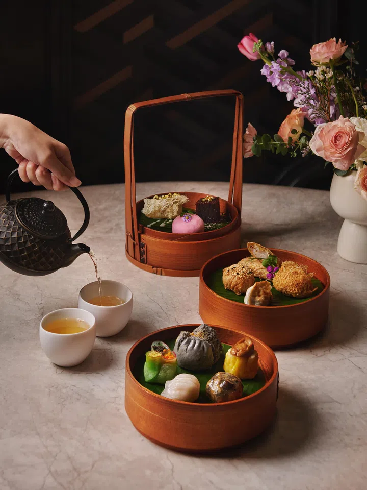 新加坡Capella Singapore Cassia中式点心下午茶，木质蒸笼盛装精致点心如烧卖、小笼包与创意点心，搭配茶壶与茶杯倒茶场景，呈现优雅中式下午茶氛围