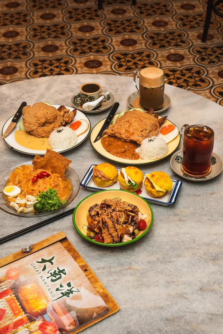 Great Nanyang Heritage Café 餐桌合照，桌上摆放多道本地经典料理，包括海南鸡扒配饭、叻沙、迷你菠萝包以及南洋咖啡与茶饮|新加坡最值得打卡的高颜值聚餐好去处，呈现结合怀旧风格与本地美食的聚餐场景，适合好友小聚与下午休憩时光。