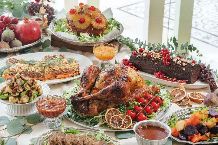 PS.Cafe 的圣诞外带盛宴摆在长桌上，包括整只金黄烤火鸡、蜜汁火腿、蜂蜜味噌芥末烤三文鱼、布鲁塞尔芽菜、烤根茎蔬菜、配酱，以及巧克力树桐蛋糕等多款节庆料理。2025圣诞外带套餐推荐：在家享用超值又美味的圣诞大餐