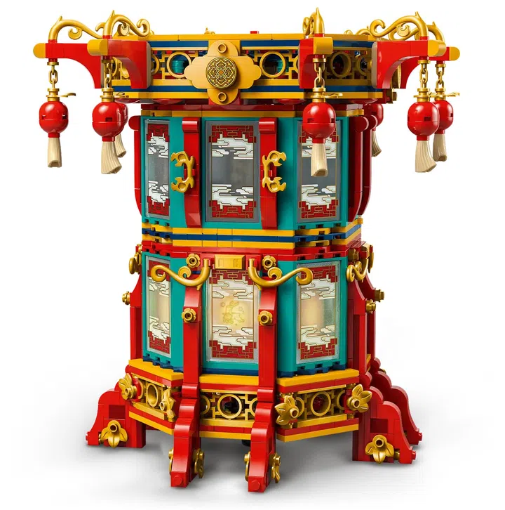画面展示 LEGO「福来运转灯」（Trotting Lantern，80116）积木灯笼模型。整体为多层八角形灯笼结构，以红色、金色与蓝绿色积木拼接而成，外框装饰大量中式卷纹与花纹细节。灯笼上层四角悬挂红色圆形小灯笼与流苏吊饰，顶部以金色装饰件点缀，呈现传统节庆风格。灯体侧面设有多扇仿窗格结构的透明面板，内部可透出柔和灯光效果。底座结构稳固，搭配金色装饰元素与立体支脚设计，使整体更具层次感与建筑感。背景为纯白底，突出灯笼的色彩与细节。这款积木灯笼适合作为农历新年居家空间或展示柜中的节庆装饰摆设。
