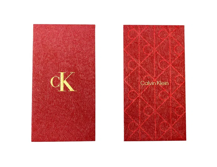 Calvin Klein 2026马年红包封正反面设计展示，红包封整体采用经典红色底色，呈现细腻的纸质纹理，营造低调而优雅的视觉效果。正面中央印有金色“ck”品牌标志，设计简洁醒目，展现品牌标志性极简风格。背面则融入压纹图案设计，以重复排列的字母元素形成几何图腾纹样，并印有“Calvin Klein”金色品牌字样，增添层次感与质感。整体设计延续品牌一贯的现代极简美学，同时融入农历新年的喜庆色彩，呈现精致且具有收藏价值的新年红包封。2026马年红包封盘点：今年的新年红包设计，你最喜欢哪一个？