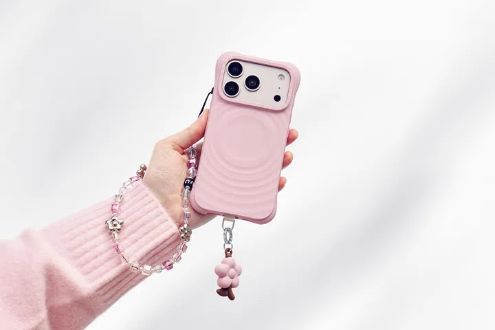 CASETiFY Spring in Bloom 系列手机壳产品照，画面中一只手拿着粉色 Ripple Case 手机壳，搭配花朵吊饰与粉色串珠手机链，整体以柔和粉嫩色调呈现春日氛围。手机壳采用立体波纹设计，展现简约又带有时尚感的风格，搭配可爱配件后更具个性与少女感，非常适合作为母亲节送给妈妈的时尚科技礼物。母亲节礼物推荐2026：从实用家居到时尚科技，这些礼物妈妈真的超爱！