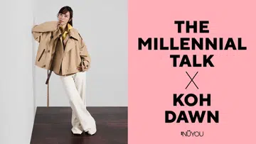 画面左侧，一位女性站在深色木地板上，背景为简洁的浅灰色墙面，整体画面干净利落。她将一只手轻靠在下巴处，身体微微侧倾，姿态随性又带点思考感，眼神直视镜头，神情沉稳而自信。她穿着卡其色宽松外套，内搭亮黄色上衣，下身搭配米白色长裤与浅色高跟鞋，整体造型以中性色为主，点缀亮色，展现出利落又不失个性的时尚风格。右侧为粉色背景，上面以黑色大字写着“The Millennial Talk X Koh Dawn”，下方为《女友》（NÜYOU）标志，整体视觉简洁现代，突显人物专访主题。