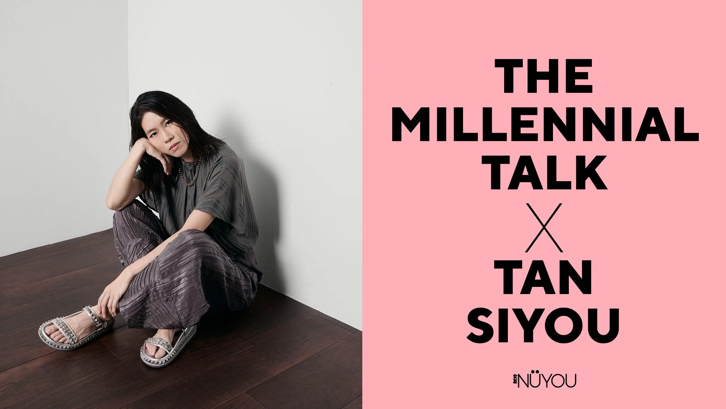 一张《女友》The Millennial Talk人物专题视觉图。画面左侧是一位留着及肩黑色长发的女生坐在白色墙角与深色木地板交接处，身体微微蜷曲，一只手托着脸侧，姿态放松自然，神情平静而若有所思地看向镜头。她身穿灰色宽松上衣，搭配深灰紫色压褶宽裤，并佩戴银色链条项链，脚穿银白色铆钉细节凉鞋。整体穿搭以低饱和灰调为主，呈现简约、中性且带有随性感的风格。人物背后形成柔和阴影，为画面增添层次与情绪感。
画面右侧为粉色背景，并以黑色大字写上“The Millennial Talk × Tan Siyou”，下方附有《女友》NUYOU标志。整体视觉风格简洁利落，同时带有安静、内敛且富有故事感的人物专题氛围。