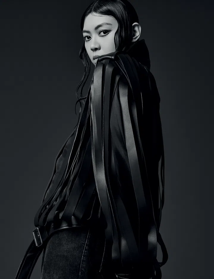 Jasmine Sokko穿着LOEWE皮革流苏外套，长条状皮革元素垂落肩头，搭配深色牛仔裤。她微微转身，眼神凌厉，营造神秘又前卫的氛围。