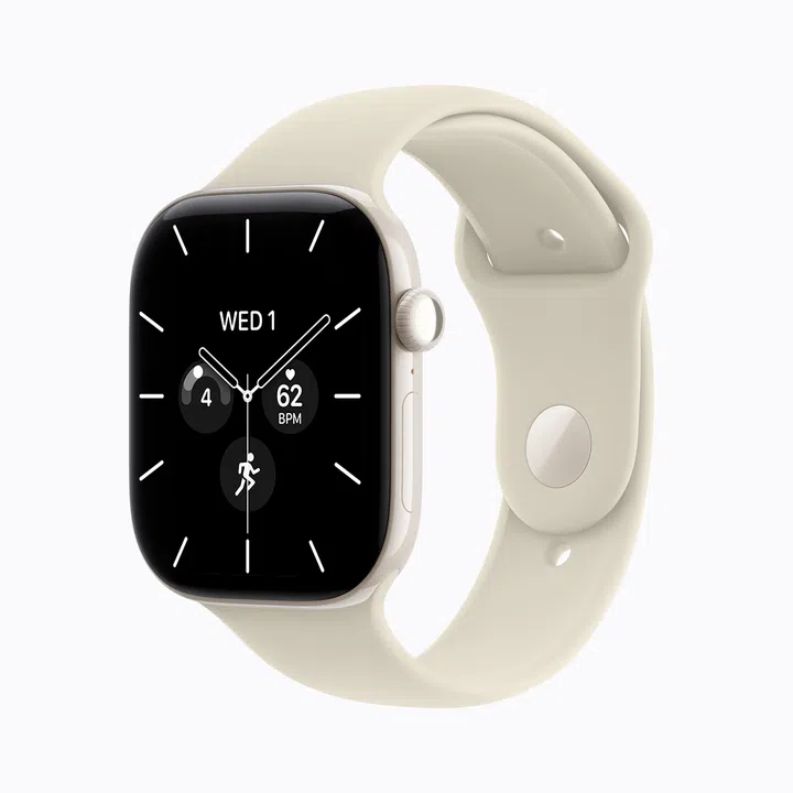 Apple Watch Series 12珍珠白色Pearl White陶瓷款产品图，搭配浅米色Sand运动型表带。手表以斜侧角度展示，黑色表盘采用简约指针设计，并显示“WED 1”日期、每分钟62次心率及运动等资讯；右侧可见数码表冠与侧边按键。珍珠白陶瓷表壳与浅色表带相互呼应，整体呈现清爽简洁的外观。