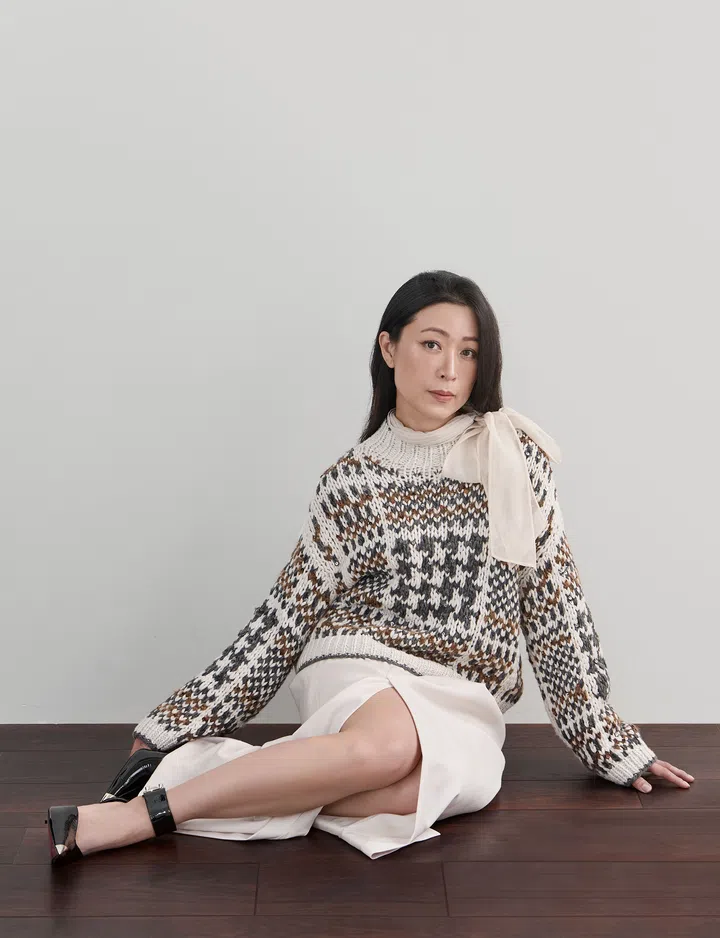 Cheryl Han身穿格纹毛衣与白色裙装，坐在木质地板上，直视镜头，展现自然自信的气质。The Millennial Talk Cheryl Han， on.wellbeing, PROLOGUE, hunter and match。