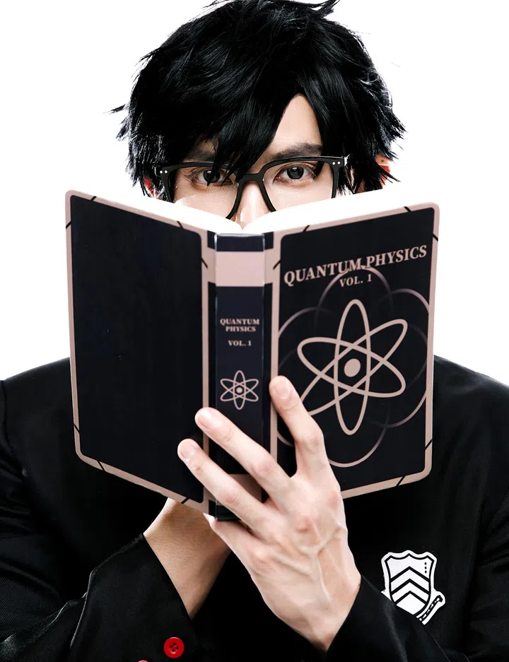 一名戴着黑框眼镜的年轻人，留着凌乱感的黑色短发，双眼从一本打开的书本上方望向镜头，只露出上半张脸，神情专注而冷静。他双手捧着一本深色封面的书，书名为「QUANTUM PHYSICS VOL. 1」，封面设计以简约的原子图案为主，整体呈现黑色与浅色线条的对比。人物身穿黑色外套，左胸位置有白色徽章图案，袖口可见一颗红色钮扣细节。背景为纯白色，光线明亮且均匀，使人物轮廓与书本细节更加清晰，整体画面营造出理性、知性、带点神秘感的视觉氛围，像是在阅读或思考复杂知识内容的瞬间。kazuya cosplay personal 5雨宫莲 joker 角色扮演 