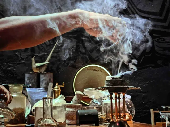 一只手悬在燃香炉上方，香气缓缓升腾，烟雾在空气中缭绕；桌上摆放着玻璃瓶、金属器具与香料，营造出浓厚的古老与神秘氛围。哪里可以用SG Culture Pass？文化通行证活动推荐