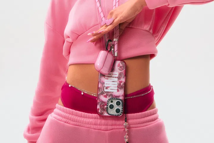 一位身穿粉色运动套装的女性，手上戴着粉色蝴蝶戒指，手机壳为粉色图案设计，搭配粉色挂绳与耳机壳，整体造型展现统一的粉色风格，时尚又个性。CASETiFY iPhone16手机壳，粉色时尚。高颜值手机壳推荐。