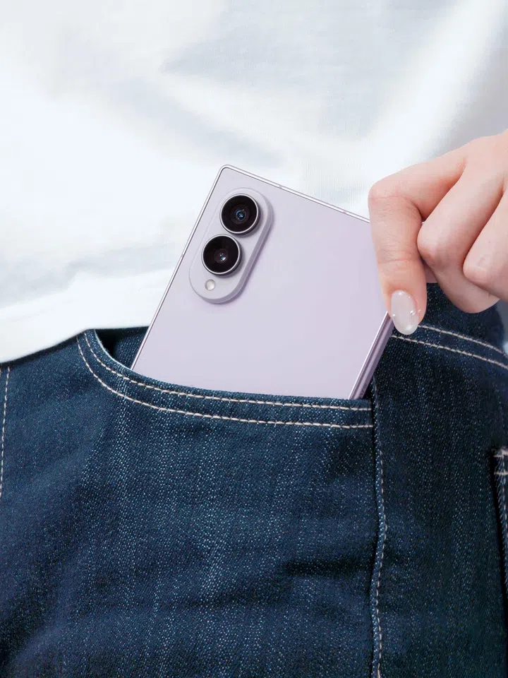 一只手正将Samsung Galaxy Z Fold8 Lavender（薰衣草紫）放入口袋，展示折叠状态下的轻薄机身与便携设计。手机露出上半部机身，可见雾面淡紫色背板、双镜头相机模组及LED闪光灯，整体设计简约精致。人物身穿白色上衣及深蓝色牛仔裤，手指轻握手机边缘，呈现日常将手机收进口袋的使用情境。画面重点突显Galaxy Z Fold8折叠后的轻巧尺寸、纤薄机身及方便随身携带的特性，展现适合日常通勤、外出及移动办公的使用体验。
