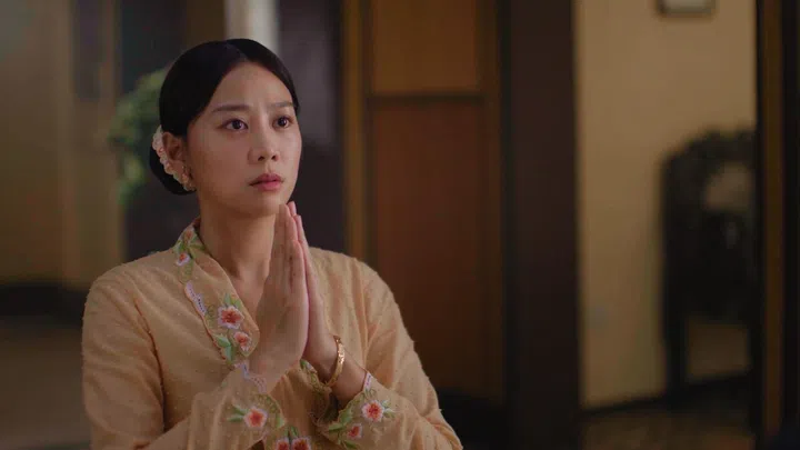 刘怡伶在《小娘惹之翡翠山》中的一幕情绪戏，身穿米色刺绣娘惹服的她双手合十，神情紧张而虔诚，眼神中带着不安与期待。她的发型低盘整齐，搭配传统饰品，整体造型温婉典雅。画面置于室内场景，暖色灯光与木质空间营造出沉静氛围，镜头聚焦她细腻的面部表情，突显角色在关键时刻的心理波动与情感张。红星大奖2026《最佳女主角》入围者
