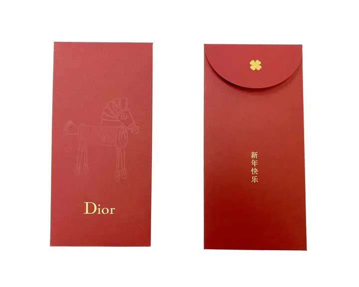 Dior 2026马年红包封正反面设计展示，红包封整体采用柔和深红色调，并以细腻纸张质感呈现品牌一贯的优雅风格。正面中央压印一匹线条简洁的骏马图案，以低调压纹方式呈现，在光线下隐约浮现，展现细致工艺与含蓄美感，下方印有“Dior”金色品牌标志，提升整体精致度与品牌辨识度。背面采用翻盖信封设计，中央以金色烫印呈现“新年快乐”字样，象征节庆祝福，翻盖上方则饰有小巧的金色花卉装饰元素，为整体设计增添优雅细节。整体设计融合简约现代美学与传统新年寓意，在低调中展现高级质感与品牌风格。2026马年红包封盘点：今年的新年红包设计，你最喜欢哪一个？