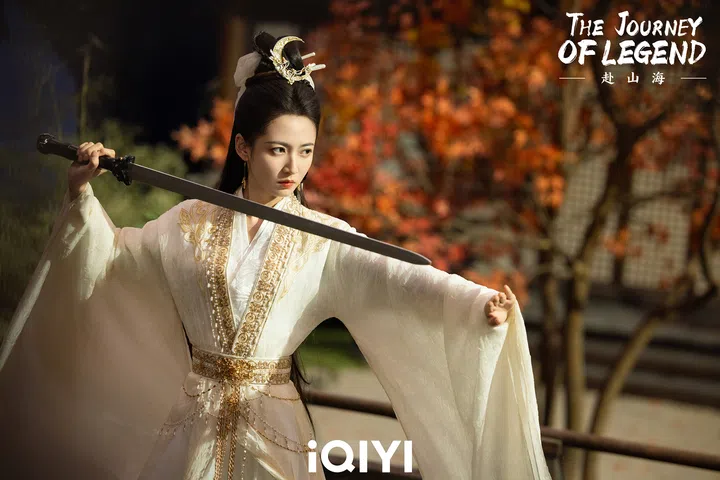 身着白色绣金长袍的女子在秋日场景中持剑出鞘，画面展现古装剧的武侠氛围与力量感。《赴山海》剧照