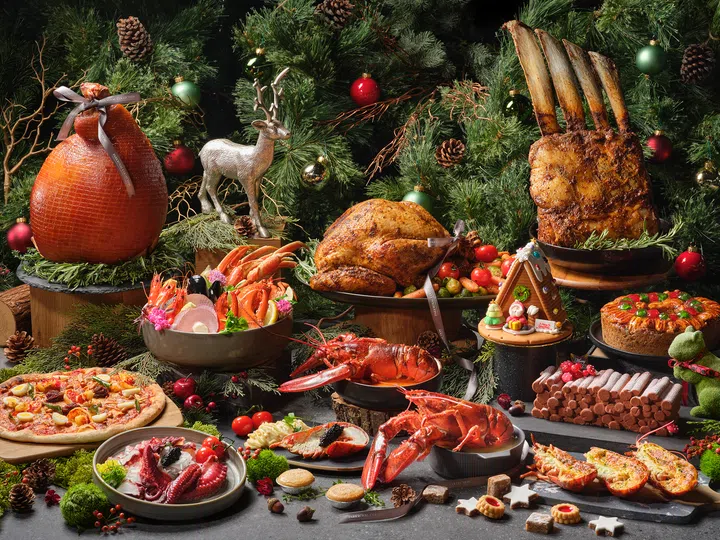 木盘上摆满圣诞主题的水果、奶酪、冷切肉、坚果、甜点和装饰小糖果，周围点缀松果与圣诞绿叶，整体呈现温暖又充满节庆气氛的圣诞拼盘画面。圣诞大餐吃什么？新加坡9家必订自助餐全攻略