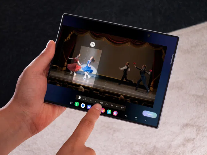一名用户双手握着展开状态的Samsung Galaxy Z Fold8，正在使用Galaxy AI的My FanCam功能观看舞台演出影片。手机大尺寸内屏播放一场剧院表演，画面中央以智能追踪方式自动放大聚焦一位身穿蓝色洋装的舞者，其他演员则维持在完整舞台画面中，方便用户专注观看指定人物的演出。屏幕下方可见多种画面比例选项及操作工具列，右下角则显示“Follow”按钮，展示My FanCam能够自动追踪画面中的人物并重新构图。整体画面突显Galaxy Z Fold8大屏幕结合Galaxy AI功能，在观看演唱会、舞台剧或运动赛事时，带来更灵活、更沉浸的观赏体验。