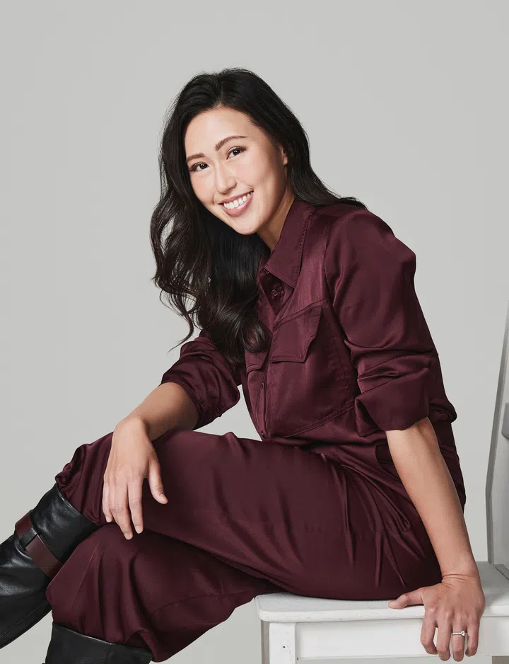 《The Singaporean Dream》桌游设计师Theresa的创作灵感，就来自你我熟悉的新加坡生活点滴。Theresa，身穿酒红色连身服，坐在白色椅子上，微笑望向镜头。