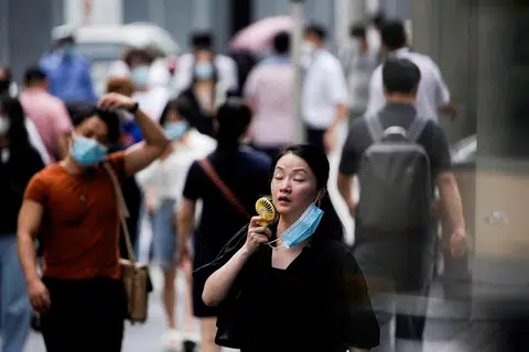天气太炎热，上海街头一名女士拿出小风扇降温。（路透社）
