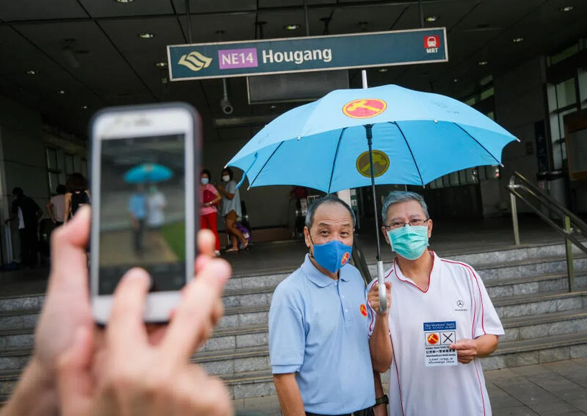  2020年大选竞选期最后一天，工人党前秘书长刘程强（左）在7月8日现身后港地铁站一带为工人党阿裕尼集选区的竞选团队助阵。工人党“粉丝”还特意带了“蓝党”招牌雨伞，请刘程强在上面签名。（联合晚报） 