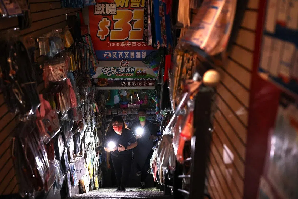 台湾民众逛街时突然遇到大停电，只好开启手机的手电筒功能走出店外。（路透社）