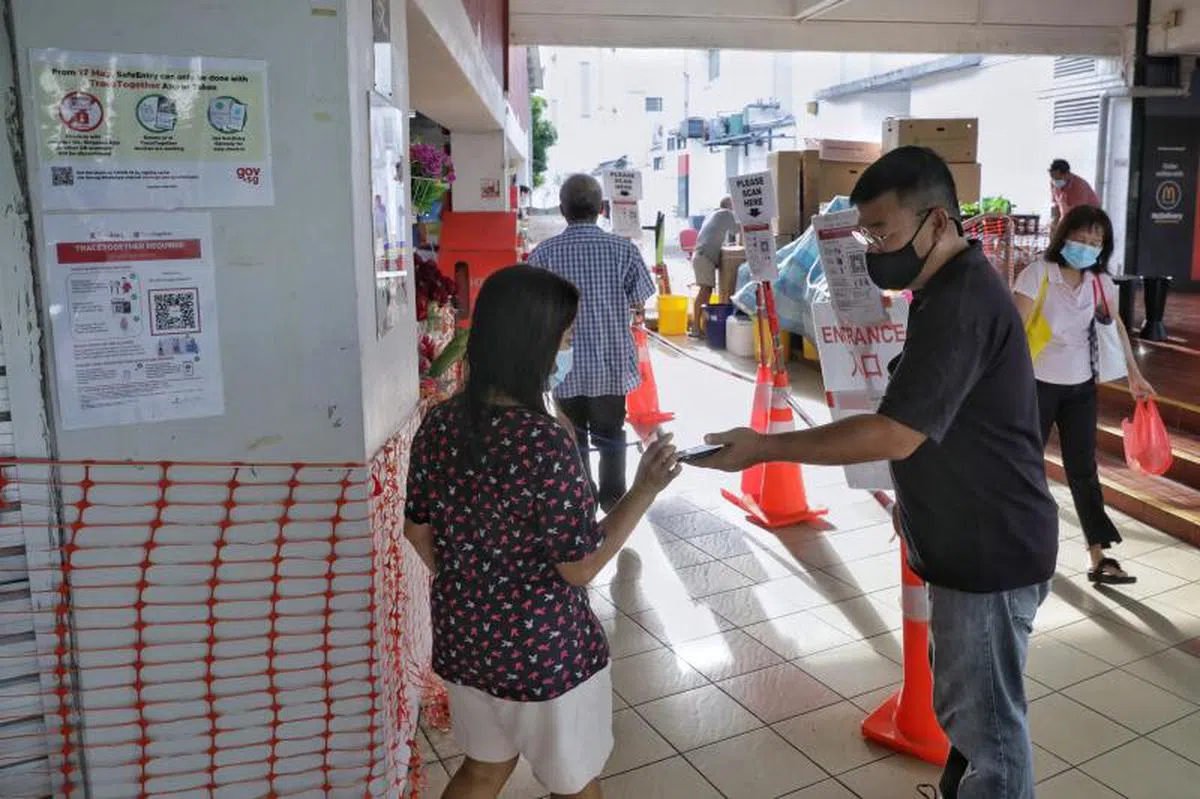  高文第209座巴刹与小贩中心的一名工作人员，正在协助来往顾客扫描“合力追踪”便携器。（海峡时报） 