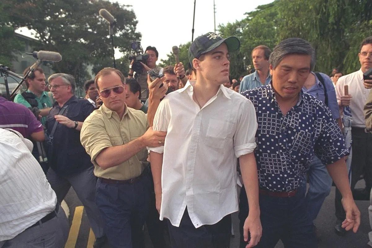  1994年6月21日上午8时20分，美国青年迈克菲（Michael Fay）踏出新加坡女皇镇拘留监狱，重获自由。迈克菲（中）出狱，立即吸引国内外新闻工作者的团团包围，他的生父乔治菲（左）和继父陈马科（右）连忙为他开路。（联合早报） 