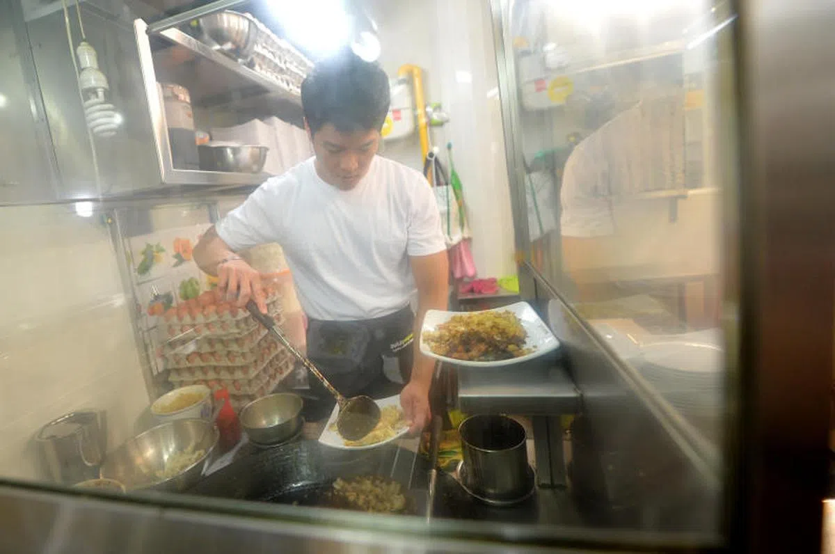  年轻小贩郑为德为了传承美食文化，毅然辞工向父亲郑启发学艺，父子同心在武吉班让小贩中心开裆卖炒粿条、菜头粿和炒福建面。（新报） 