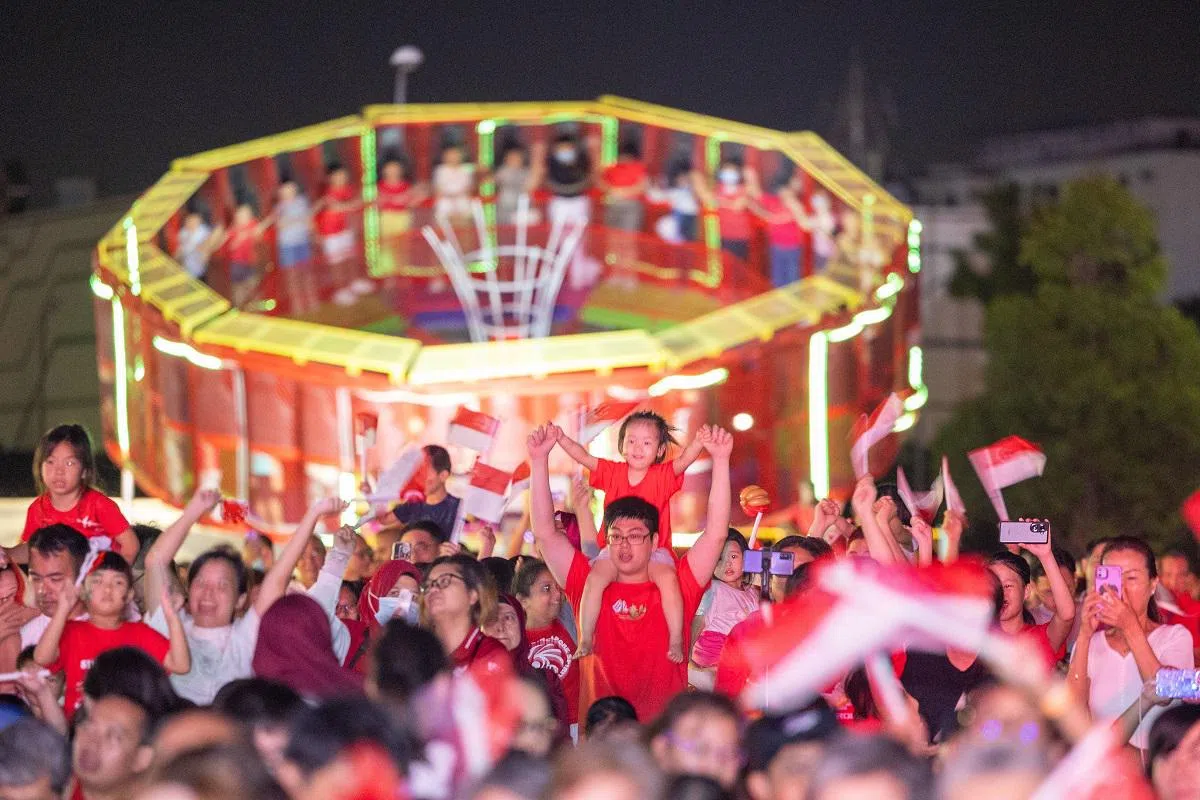 新加坡民众一边哼唱国庆主题曲一边挥着红白星月国旗，沉浸在国庆的氛围中。（联合早报）