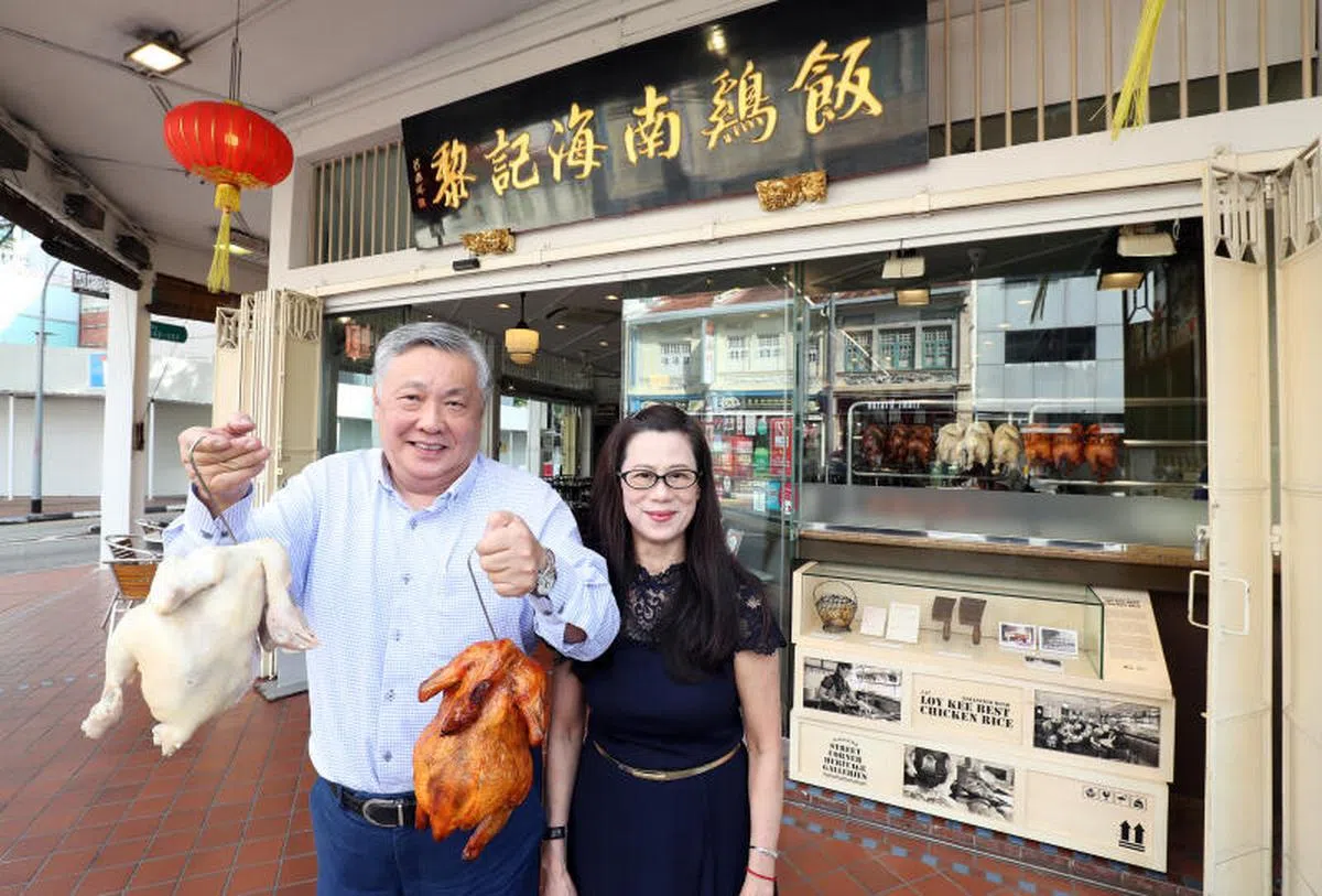  黎记海南鸡饭老板黎才忠与妻子陈丽芳在店外展示父母曾用过的菜刀（右）。（联合早报） 