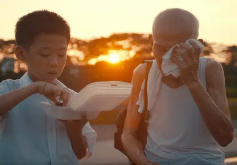 影片中的小阿成在吃鸡腿，捡纸皮的阿公在一旁擦汗。（视频截图）