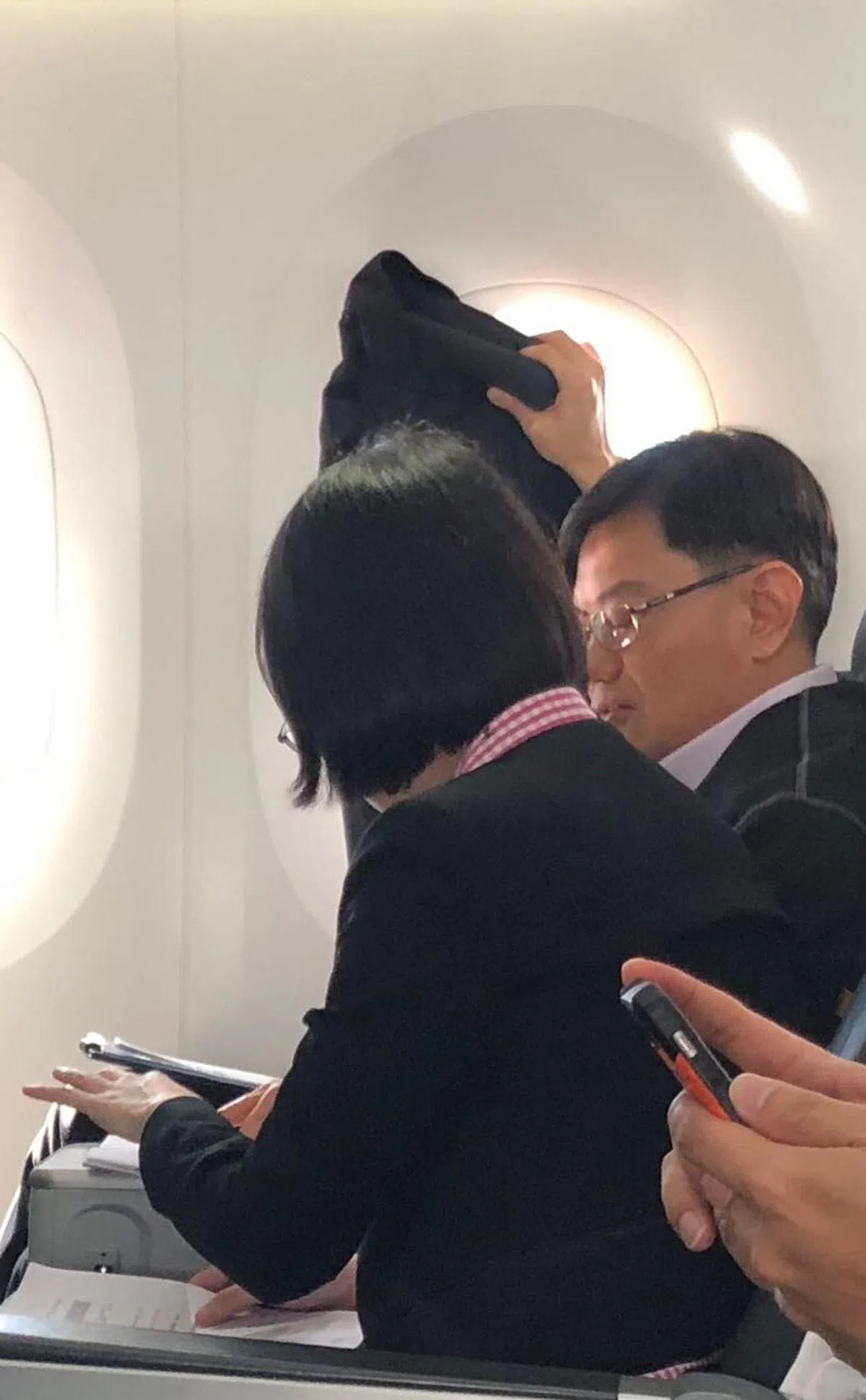  王瑞杰部长昨早坐酷航商务舱飞往南京，上机后大部分时间都在工作。当阳光太刺眼时，他右手举着西装外套挡住窗户的强光，左手继续翻看文件。坐在部长身旁的应该是财政部官员。（同机乘客提供） 