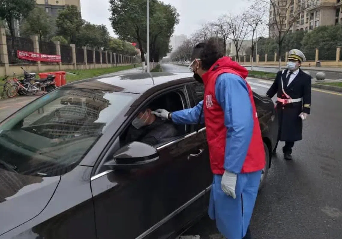 旅居中国江苏的本地动漫教师许春得加入小区志工队，穿着防护衣为进出社区的居民量体温。（许春得面簿）