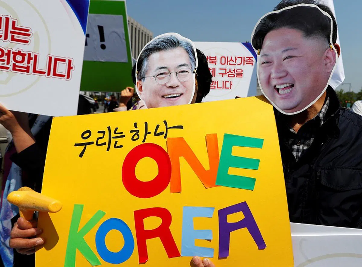  韩国民众4月25日在峰会举行前，戴上文在寅和金正恩的面具，举标语声援“韩朝统一”。（路透社） 