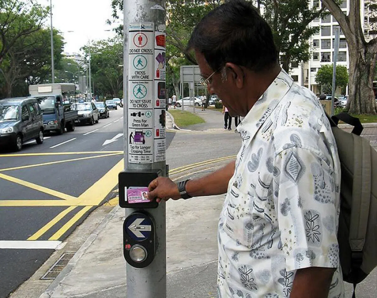  在“友善绿人计划”下，年长者和残障人士用优惠易通卡轻轻触碰交通灯柱上的四方格，就能延长过马路的“绿灯”时间。（新加坡交通部） 