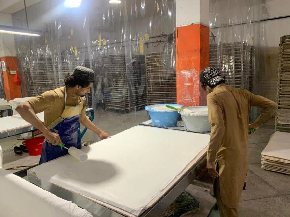 在巴基斯坦锡亚尔科特的一家足球制作工厂，工人们正在给人造革片涂上胶水。（Ziad Haider提供）