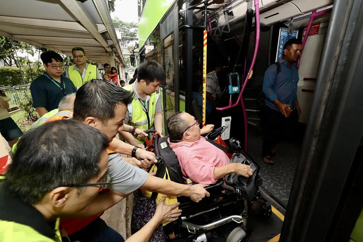 一名坐轮椅的乘客在四名工作人员的帮助下上巴士，据《联合早报》记者观察，工作人员担心巴士走动时轮椅跑偏，还细心地将轮椅乘客往里面推。（联合早报）