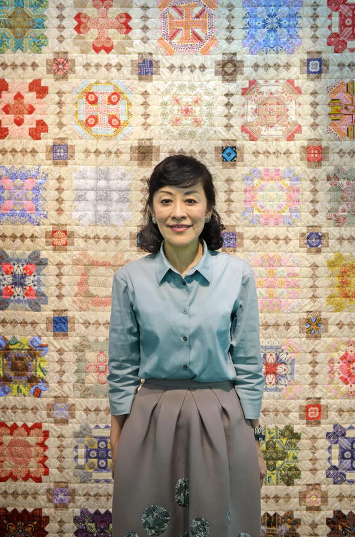  2014年林学芬摄于住家。身后挂着的就是她缝制的拼花被子。看到吗？她裙子上有几个拼花图案，据说是她自己缝上去的，既美观又可遮盖咖喱酱污渍。（海峡时报） 