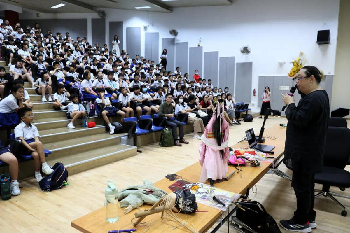 猴纸剧坊艺术总监何家伟（右）于2025年2月5日到南华小学举行偶戏分享会，并在分享会上介绍不同籍贯的趣味传统偶，令台下学生看得着迷。（联合早报）