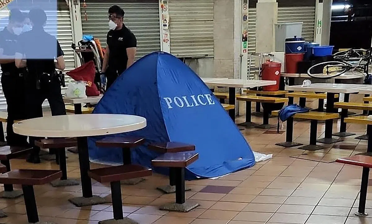 桥北巴刹与熟食中心内，睡死在餐桌上的男子被宣告死亡后，遗体被医护人员放到地上。（新明日报）