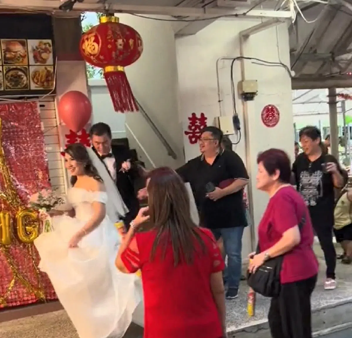 身穿婚纱和西装的新人，从麟谷峇鲁组屋楼下的走廊走进咖啡店。（视频截图）