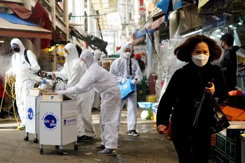 2020年2月26日，韩国首尔一个传统市场正在进行消毒工作，一名妇女戴着口罩防疫。（路透社）