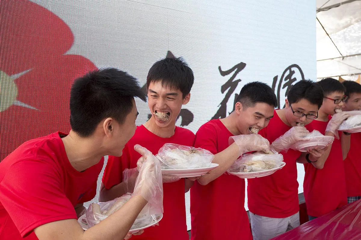 年满15岁的潮州青年在“出花园”仪式上咬鸡头，寓意独占鳌头、学业进步。（联合早报）